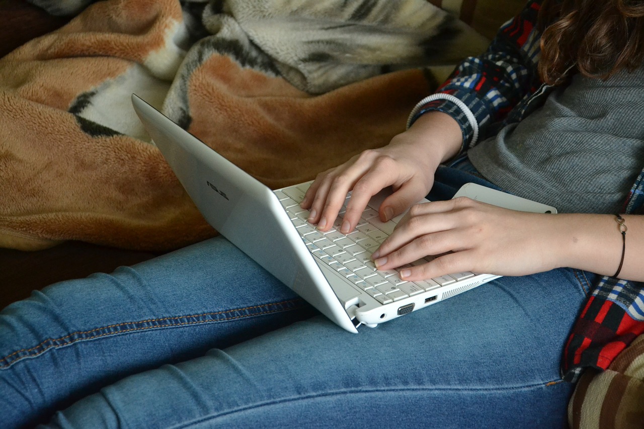 teenager typing on a white laptop