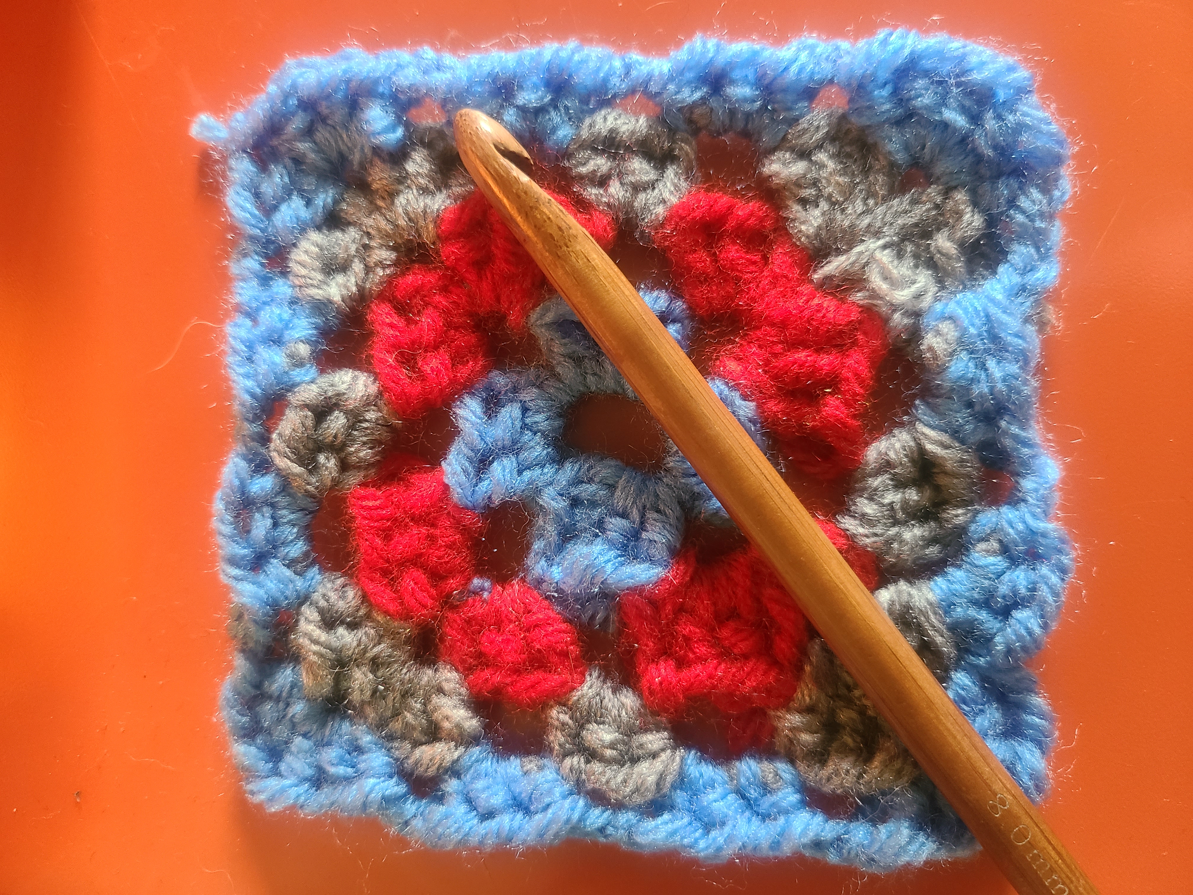 Crocheted granny square and crochet hook