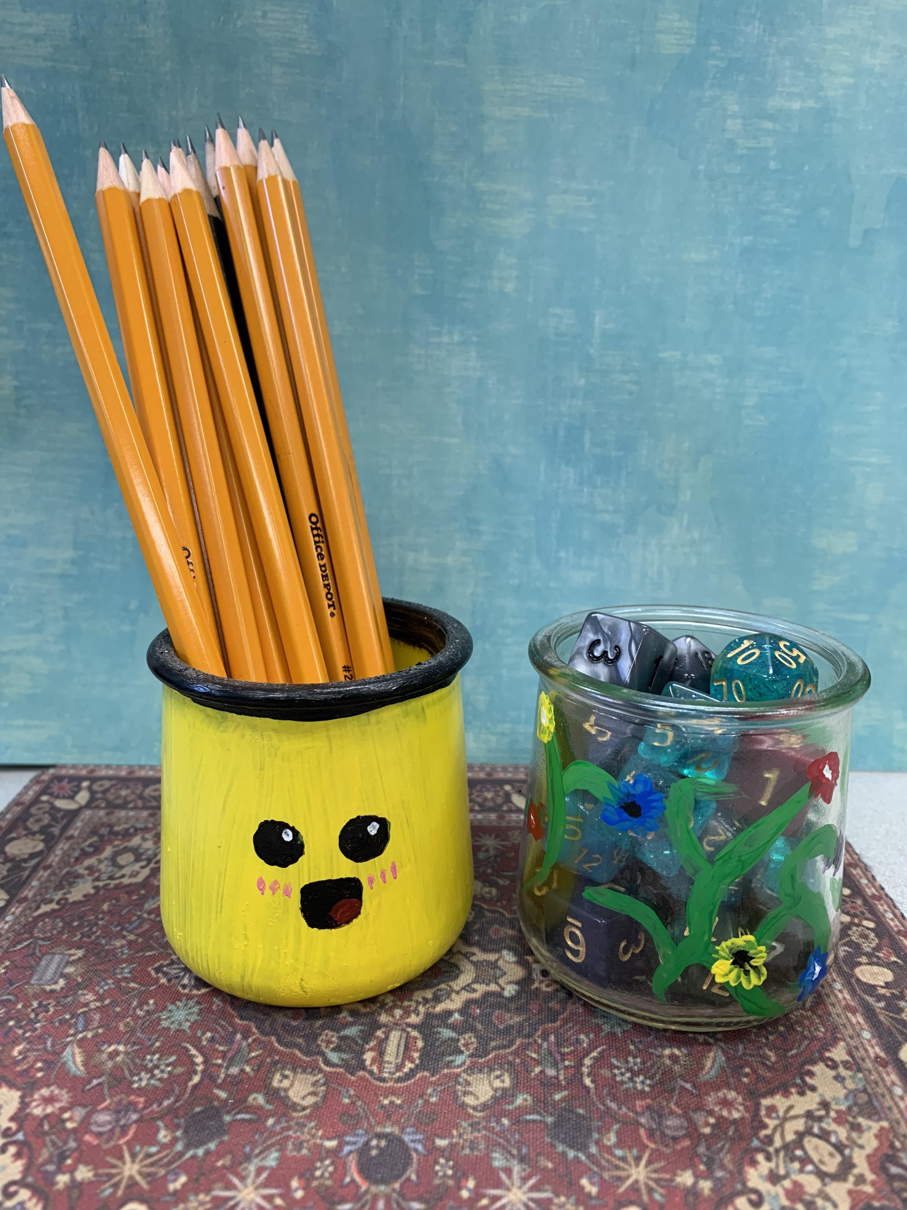 two painted jars, one with pencils in it and one with die in it.