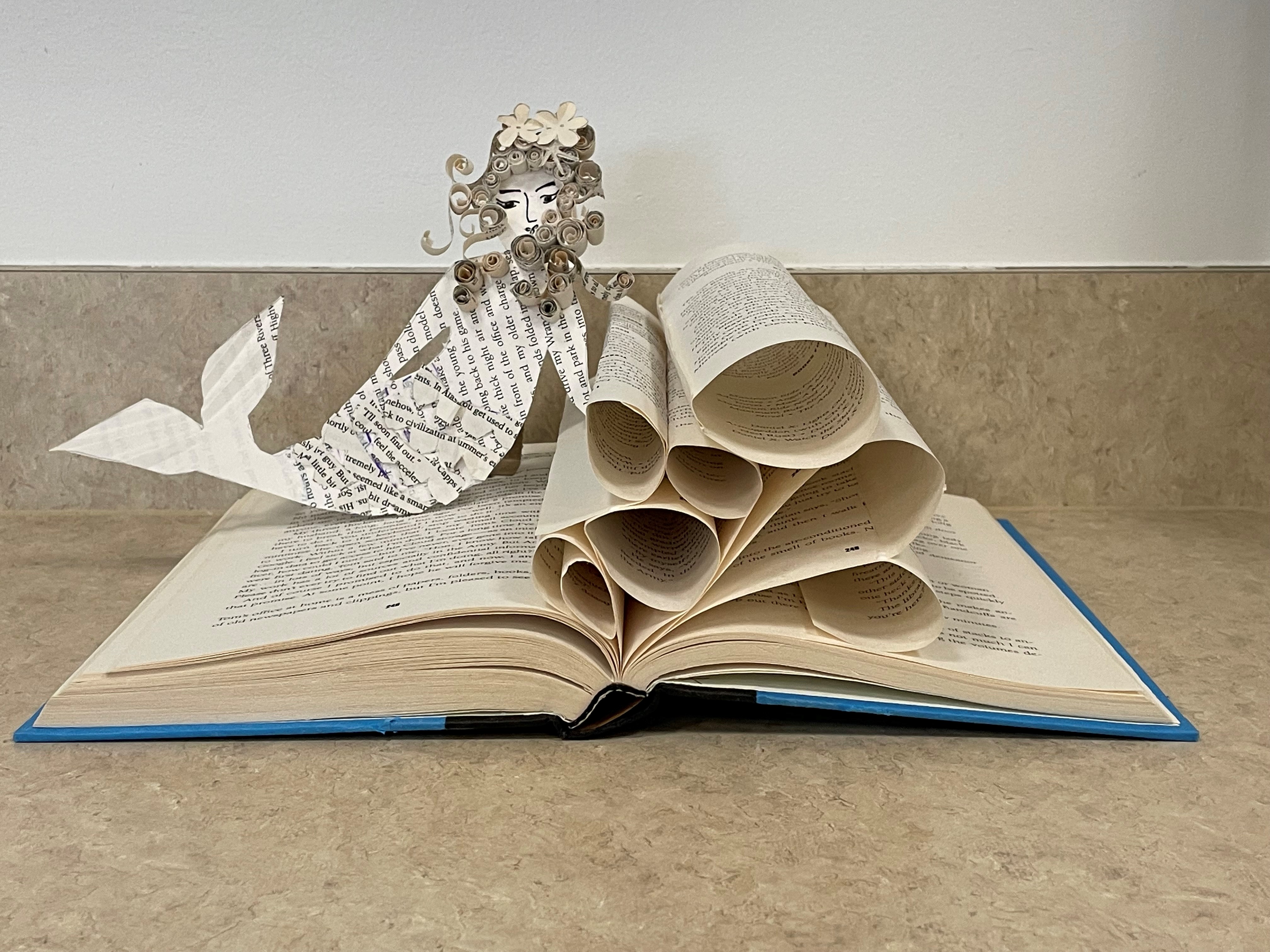 A cut-paper mermaid and waves on top of an open book