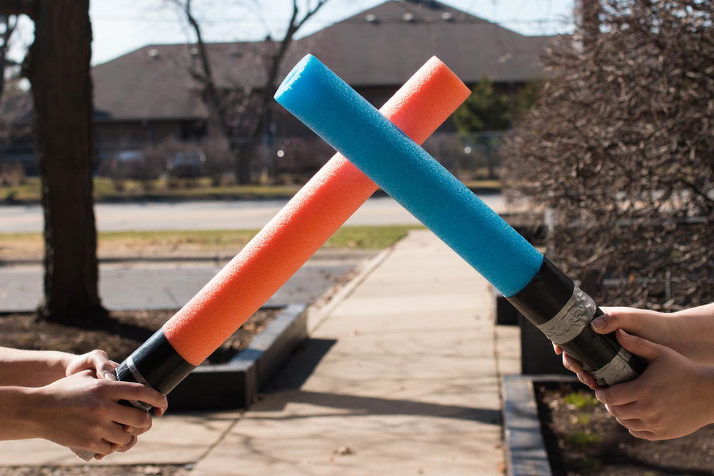 Two lightsabers made of pool noodles engaged in battle.
