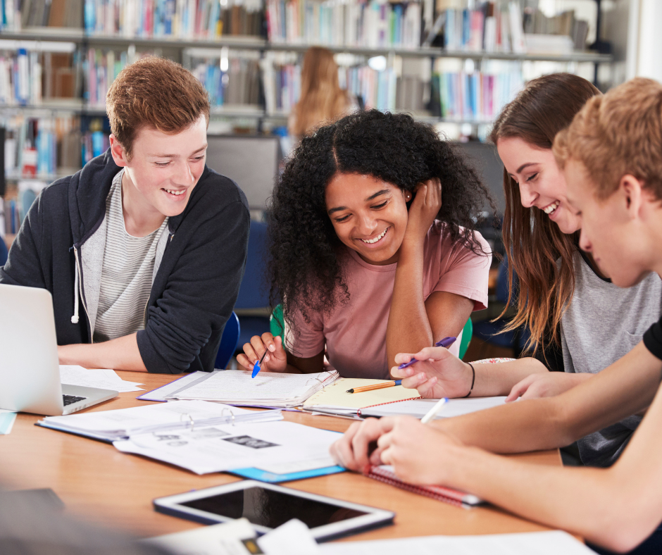 A group of teens talking at a table in a library