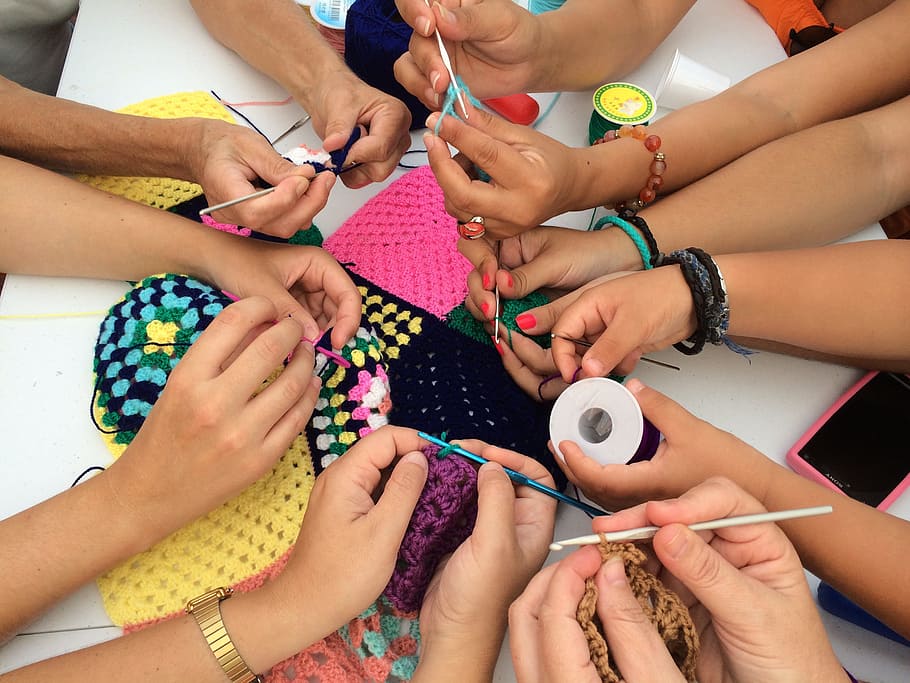 several pairs of hands working on a singular crochet project