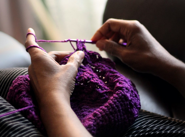close up of hands crocheting purple yarn