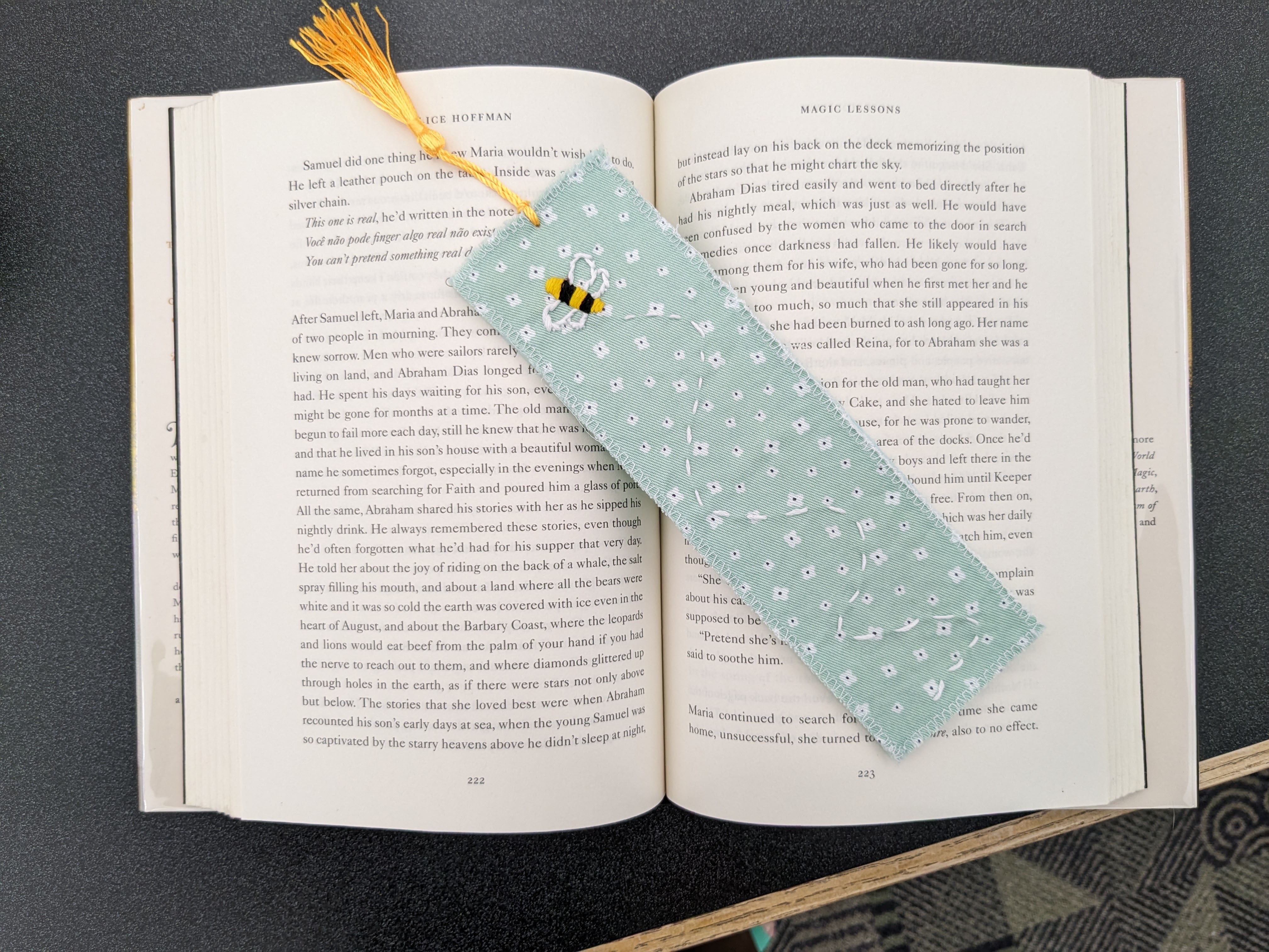 Embroidered bee bookmark with tassel on green flower fabric resting on open book
