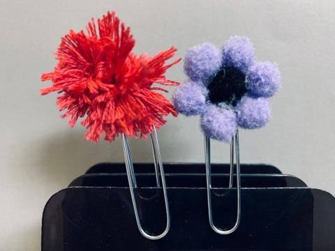 paper clip with pink string pom pom and paper clip with purple and black pom poms
