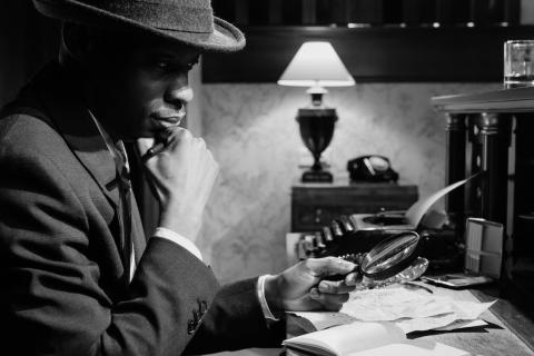 Black and white photo of a detective looking through a magnifying glass