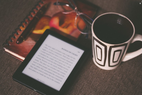 photo a Kindle sitting on top of notebook next to a mug of coffee