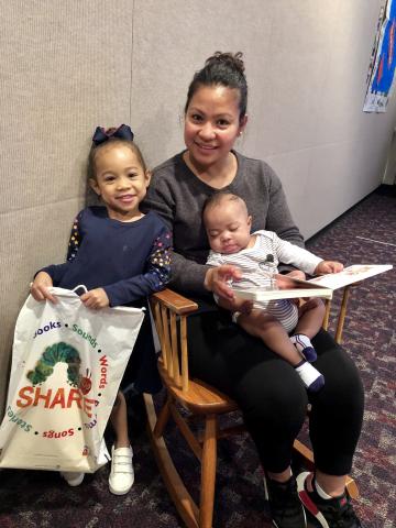 Liezel Gamiao reads to her children Haydon (age 3 months) & Haven (age 3 years) Detwiler. Haven is holding the Baby Book Bag that is given to newborns during Children's Book Week. The Baby Book Bag includes the board book they are reading.