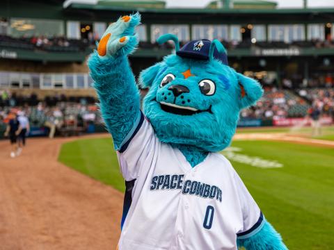 Sugar Land Space Cowboys' mascot Orion waves to a crowd in a baseball stadium.