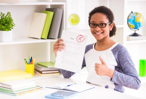 Student holding up an A+ paper in one hand and a thumbs-up with the other hand.