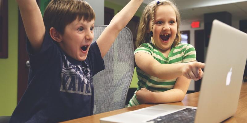 Two children cheering at computer