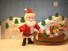 Santa marionette standing next to sleigh piled with gifts