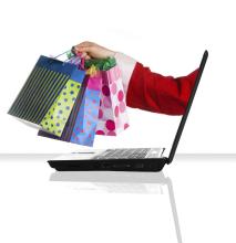 A side view of a laptop computer, with Santa's arm coming out of the screen, holding gift bags.